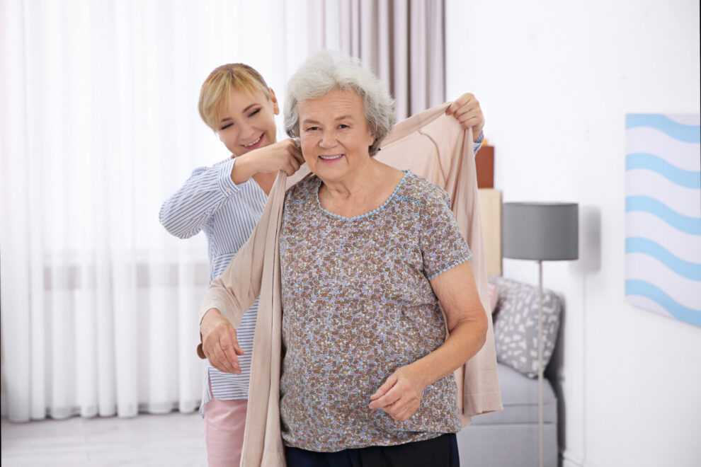 Caregiver helping senior woman to put on cardigan at home